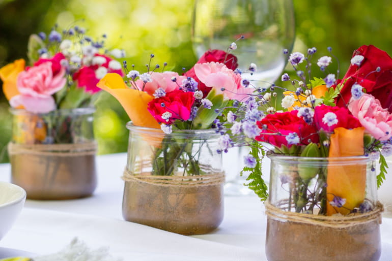 Three empty glass pots of Oui by Yoplait yogurt upcycled into flower pots. Each pot has a small arrangement of colorful flowers in them.